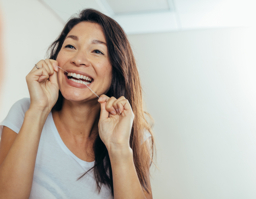 woman flossing her teeth in front of a mirror